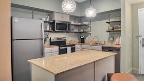 A modern kitchen with granite countertops, stainless steel appliances, and pendant lighting. - Designer 3BR/2BA Corner Suite - Disney & Universal (Orlando)