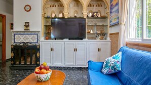 A living room with a blue sofa, a wooden coffee table with a fruit bowl, a television on a cabinet, and decorative shelves. - Pet friendly home in Doña Mencía (Doña Mencía)