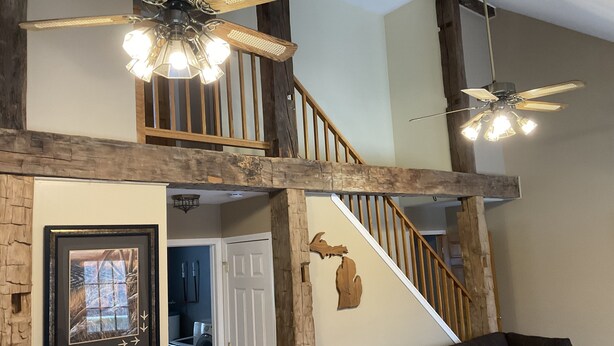 A spacious living area with a high ceiling, exposed wooden beams, a staircase, and a ceiling fan. - Cozy cabin in the woods (Evart)