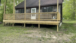 A wooden cabin with a deck, surrounded by trees. - Cozy cabin in the woods (Evart)