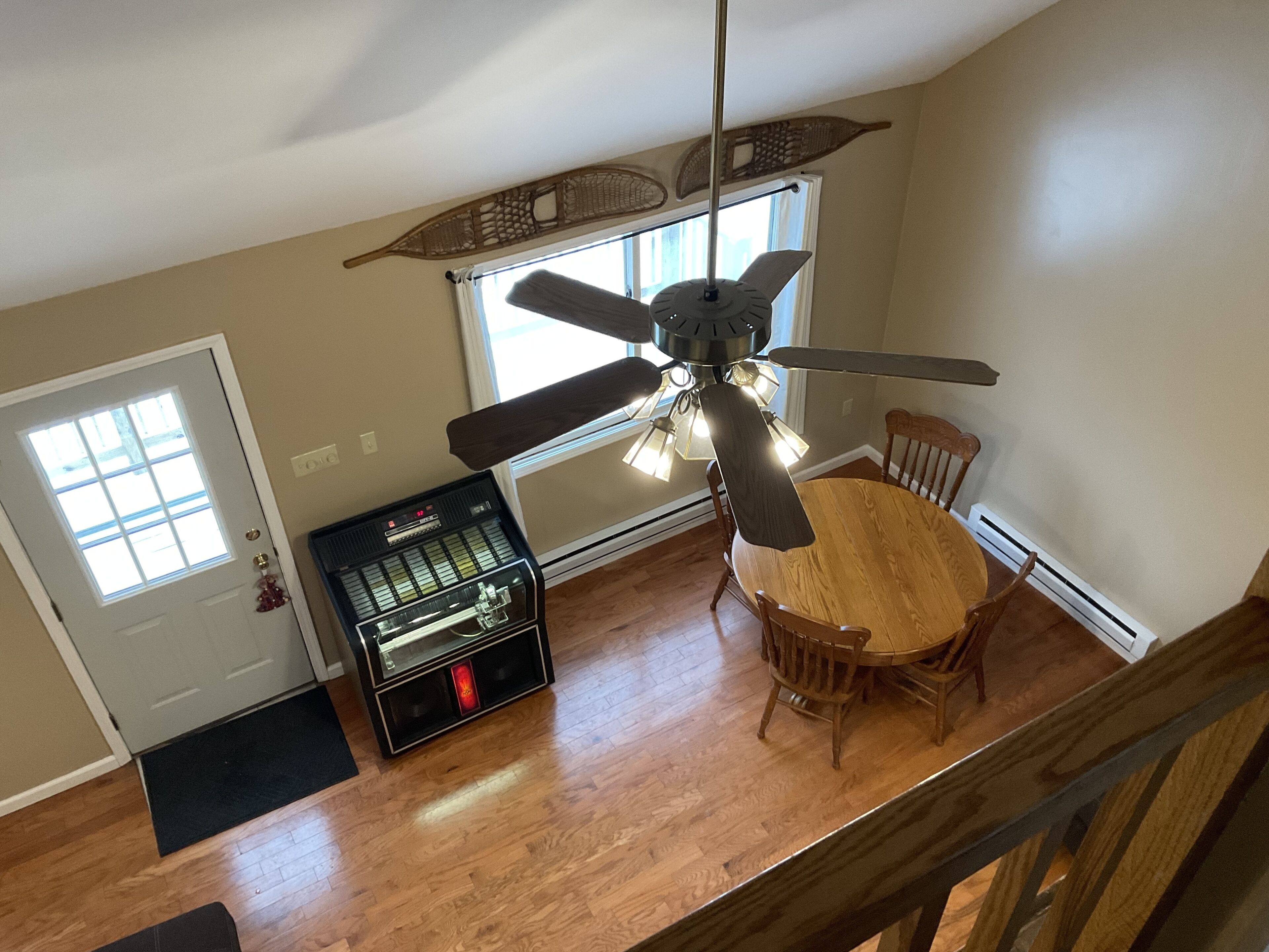 Un coin repas avec une table et des chaises en bois, un ventilateur de plafond et une radio d’époque.
