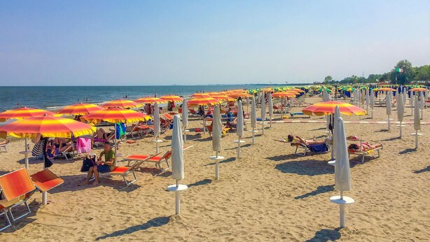 A beach with rows of orange and yellow umbrellas, beach chairs, and people relaxing.