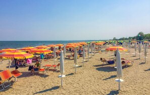 Una playa con hileras de sombrillas anaranjadas y amarillas, sillas de playa y gente relajándose.