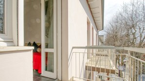 A balcony with a metal railing, a red chair, and a glass door leading to a room.