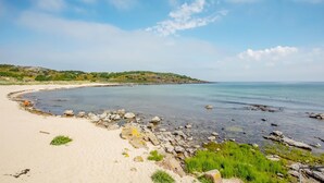 Una playa con agua cristalina, costa rocosa y una colina distante.
