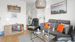 Una sala de estar moderna con un sofá gris, un sillón de cuero negro, una mesa de centro de vidrio y una lámpara colgante.