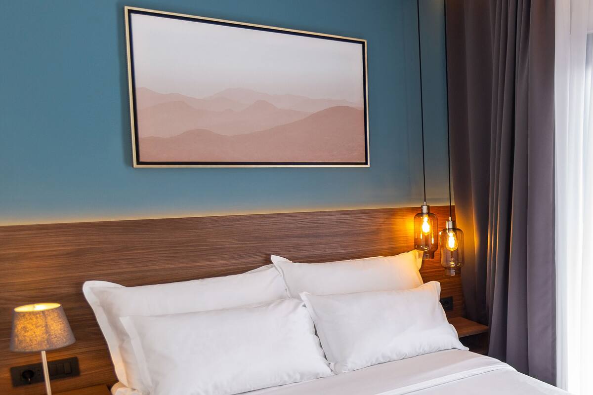 A neatly made bed with white linens, a wooden headboard, and two bedside lamps.