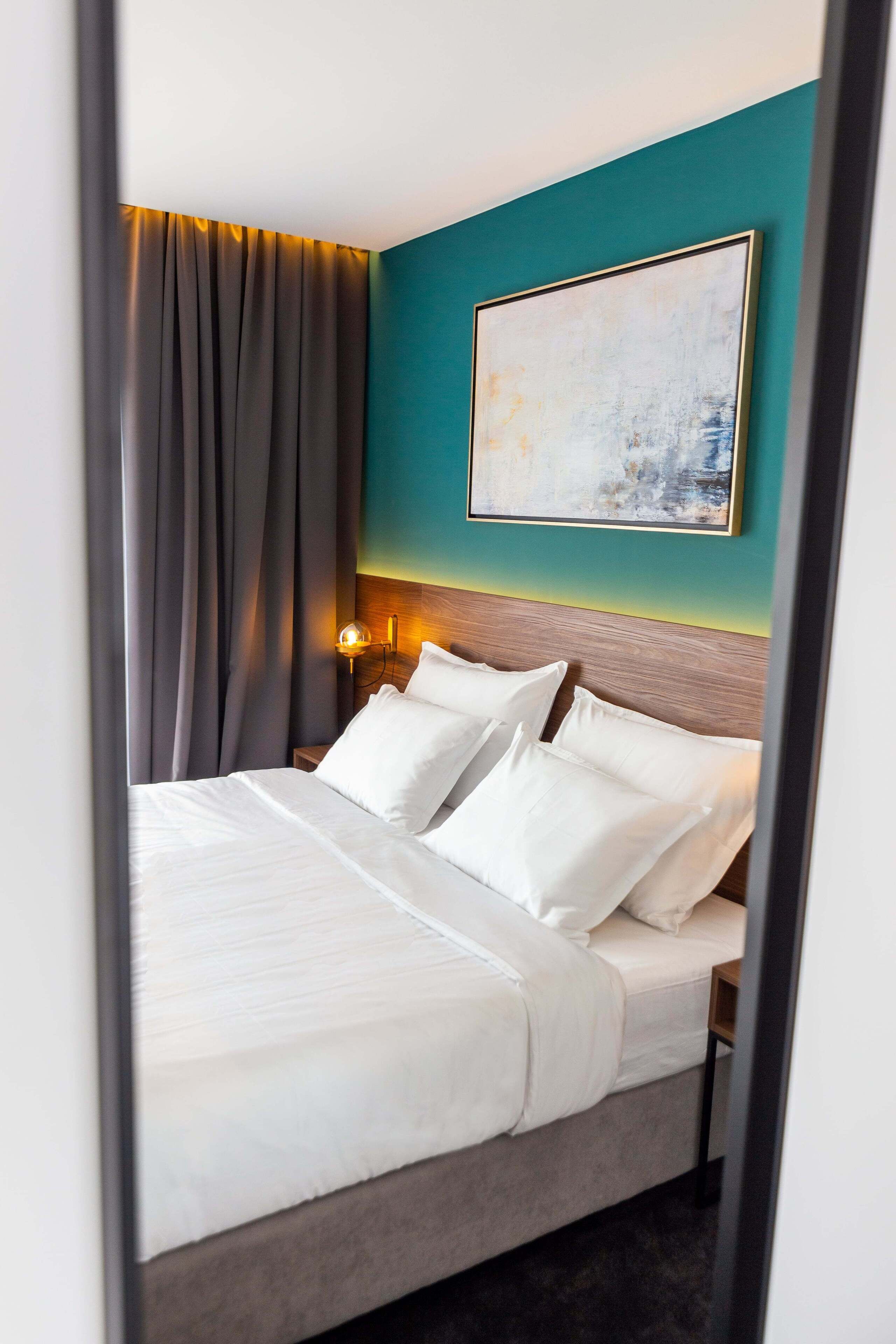 Una cama bien tendida con sábanas blancas, cabecera de madera y una pared de acento color aguamarina.