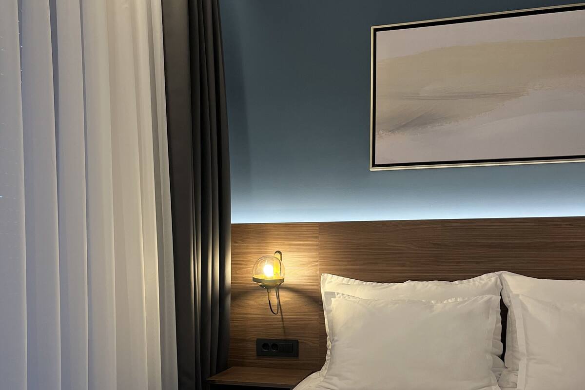 A hotel room with a neatly made bed, a bedside lamp, and a framed picture on the wall.