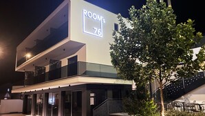 Un edificio moderno con un letrero que dice "ROOM'S 76", indicando un hotel o establecimiento de hospedaje.