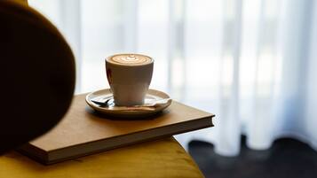 Una taza de café sobre un platito, apoyada en un libro, con una ventana al fondo.