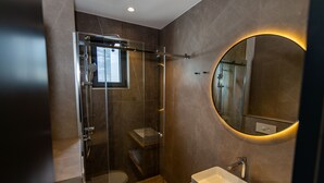 Un baño moderno con ducha de vidrio, un espejo redondo y un lavabo blanco.