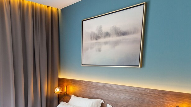 Cama doble con sábanas blancas, cabecera de madera y dos lámparas fijadas a la pared.
