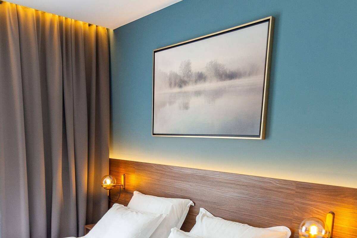 A double bed with white linens, a wooden headboard, and two wall-mounted lamps.