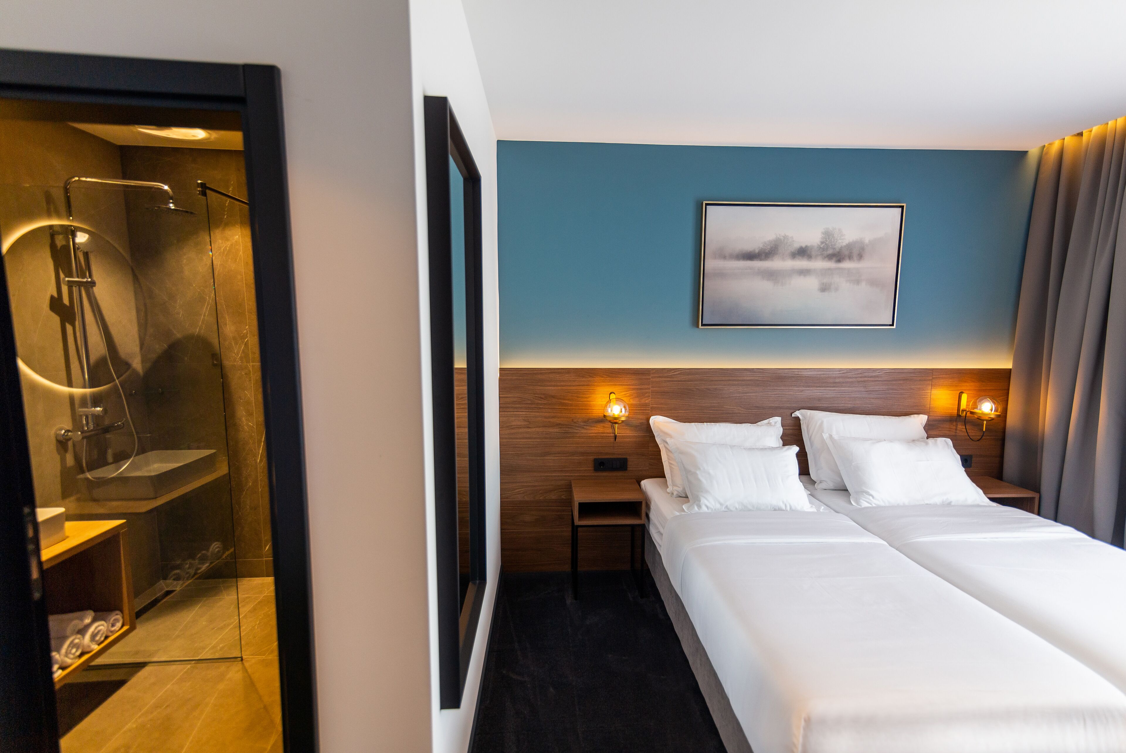 Une chambre d’hôtel comprenant un lit, des tables de chevet, un tableau accroché au mur et un espace douche.