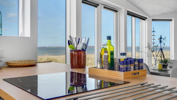 Una cocina moderna con amplios ventanales, vistas a la playa y diversos utensilios de cocina y condimentos sobre la encimera.