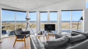 Una sala de estar moderna con ventanas amplias, un telescopio, un televisor y un sofá de cuero.
