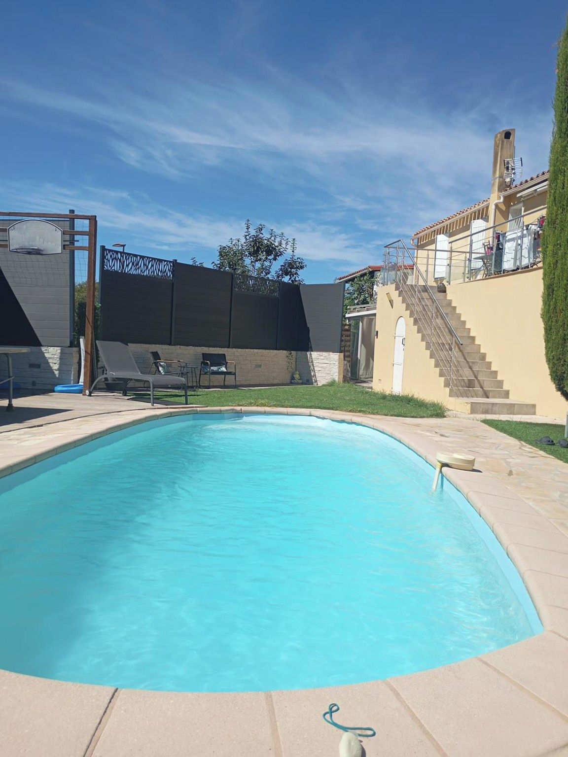 A swimming pool with a clear blue water surface, surrounded by a paved deck.