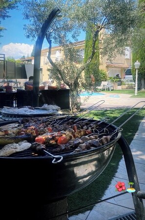 Ein Grill im Freien mit Essen, ein Schwimmbad und ein Gebäude im Hintergrund.