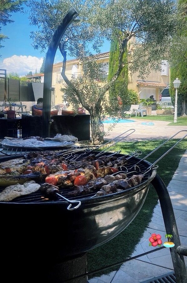 Un barbecue en plein air avec de la nourriture, une piscine et un bĂątiment en arriĂšre-plan.