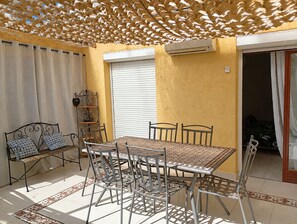 Un patio con tavolo e sedie, una panca, un muro decorativo e un condizionatore d'aria.