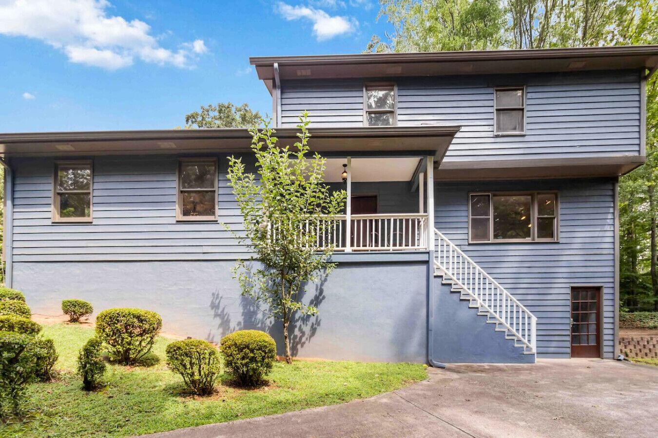 A two-story house with a front porch, a staircase, and a small garden with trimmed bushes.