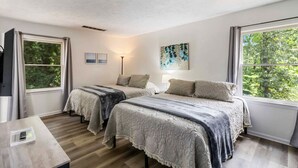 A bedroom with two beds, a bedside table, a lamp, and a painting.