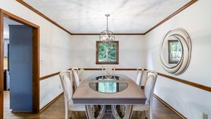 A dining room with a large table, white chairs, a chandelier, a framed picture, and a mirror on the wall.