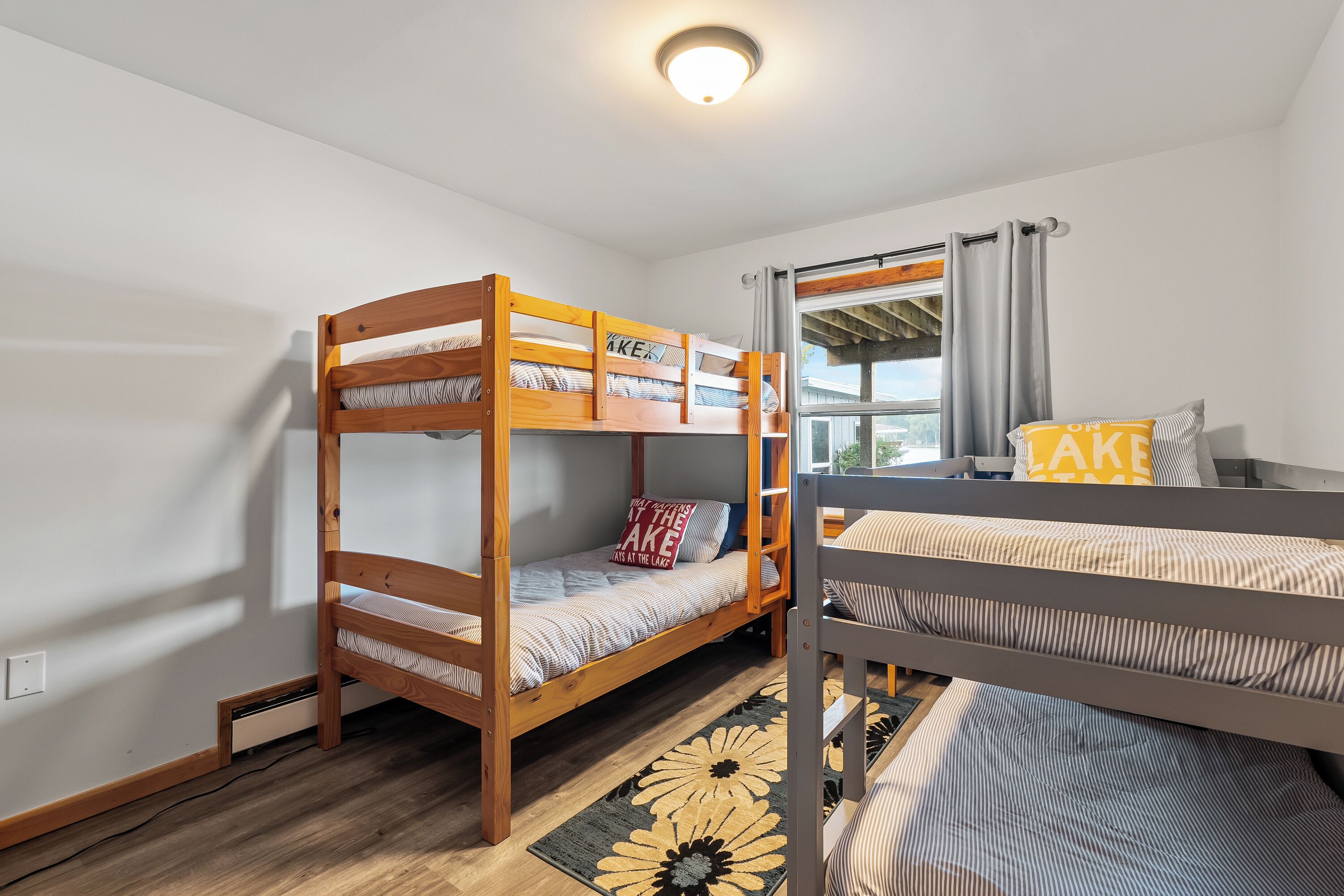 Habitación con literas, una ventana, una lámpara en el techo y un cajón pequeño debajo de la cama.