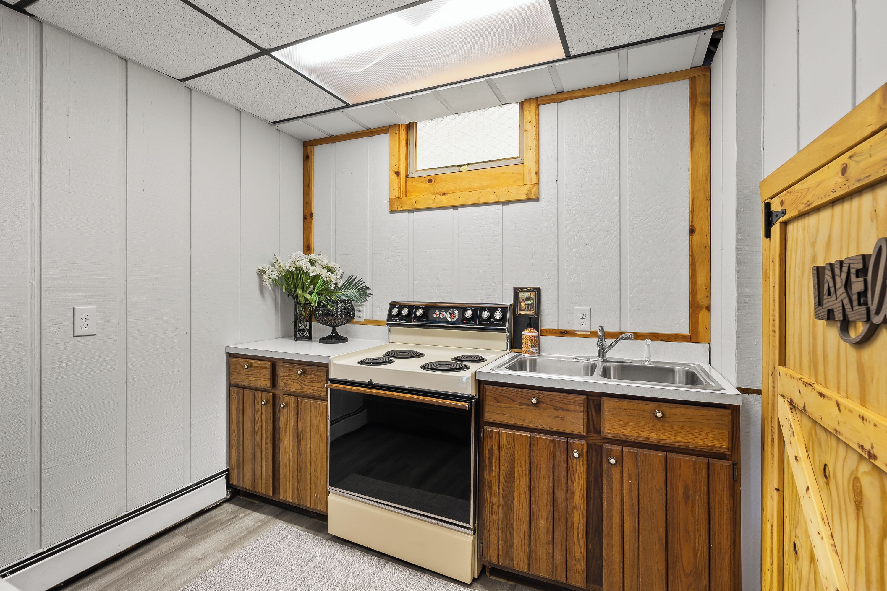 A compact kitchen with a stove, sink, wooden cabinets, and a small window.