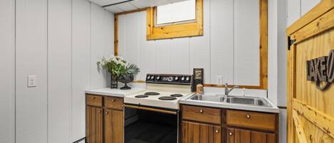 A compact kitchen with a stove, sink, wooden cabinets, and a small window.