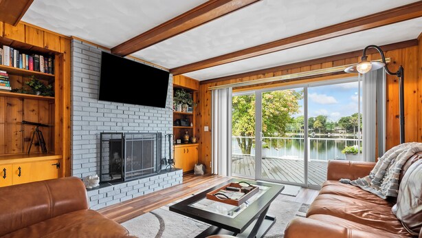 Una sala de estar acogedora con chimenea, sofás de cuero, un televisor de pantalla plana y un amplio ventanal con vista a un lago.