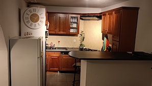 Une cuisine compacte avec des meubles en bois, une horloge intégrée et un petit îlot central.