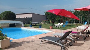 Un espace piscine avec des chaises longues et des parasols rouges, un coin salon abrité et une balançoire.