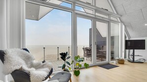 A spacious living area with a large sliding glass door leading to an outdoor balcony, a comfortable seating area with a fluffy chair and ottoman, and a flat-screen TV on a stand.