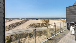 A balcony with a view of a beach, a sandy path, and a vehicle.