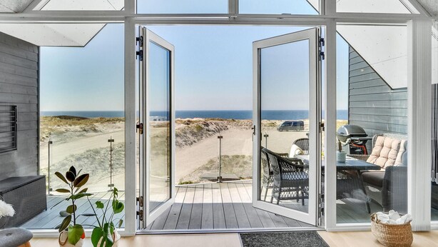 A modern interior with large glass doors leading to a deck overlooking a beach.