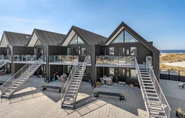 A modern building with multiple balconies, outdoor seating, and a view of the beach.