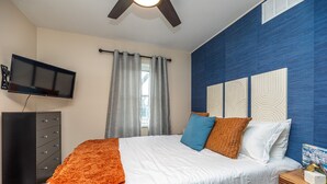 Ein Schlafzimmer mit einem Bett, einem an der Wand montierten Fernseher, einem Schminktisch und einem Nachttisch mit einem Buch.