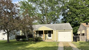 Ein Bungalow mit Garage, überdachter Veranda und gepflegtem Rasen.
