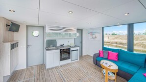 Un espace de vie compact comprenant un coin cuisine, un canapé et une fenêtre donnant sur un paysage.
