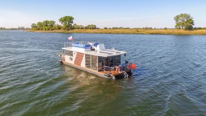 Un bateau fluvial à pont plat, arborant un drapeau et équipé de bouées de sauvetage.