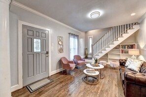 Cozy living area with a sofa, armchairs, and coffee table, featuring a staircase and bookshelf.