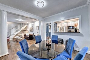 Cozy living area with a round table and four chairs, connected to a kitchen and staircase.