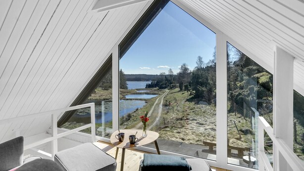 Een moderne, open kamer met een groot raam dat uitkijkt op een prachtig uitzicht over een meer en bos.