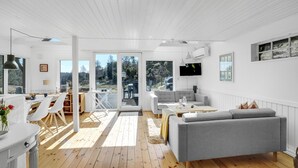 Een moderne woonkamer met een grijze bank, houten vloeren en een groot raam met uitzicht op het omliggende landschap.