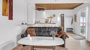 Ett modernt vardagsrum med en soffa i läder, ett soffbord i marmor och utsikt över ett kök och en matplats.