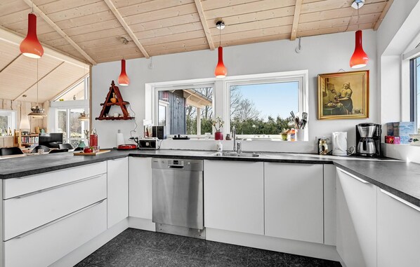 Una cucina moderna con mobili bianchi, una lavastoviglie in acciaio inossidabile e un'ampia finestra che offre vista sull'esterno.