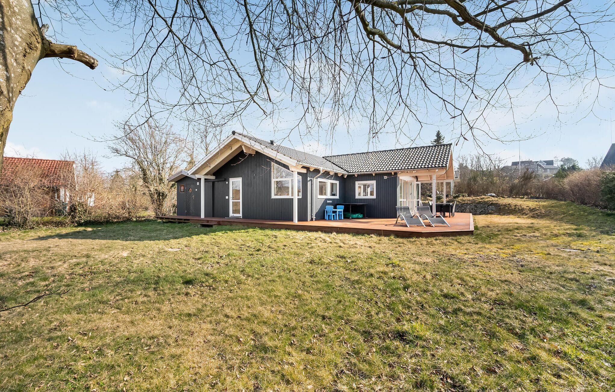 Une maison de plain-pied à l’extérieur sombre, avec un toit en tuiles et un petit porche agrémenté de deux chaises et d’une table.