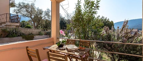 A balcony with a table and chairs, overlooking a scenic view of the sea and hills.